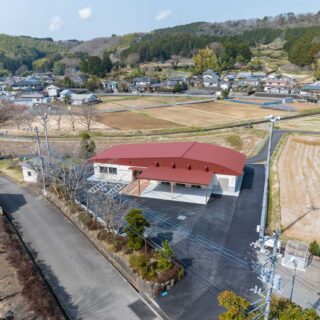 周りを山々に囲まれた山間の集落に建つ田原野公民館（東側からの外観全景）。約50世帯が集まる集落の中心部に位置し、田畑に囲まれたのどかな環境が広がる