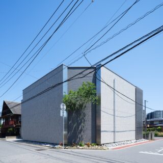 外壁には塗り替えのメンテナンスが不要な磁器質タイルを採用した。ライトグレーの壁が通りに沿って伸び、隅切り部分は壁をへこませた上でタイルの素材感と色を変え、視覚的な奥行きを生んでいる。