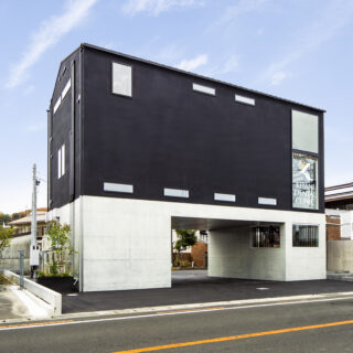 外観。建物の長辺に対しては表裏に道路が走っており、また隣家との距離もあることからすべての面の外壁が見える。そこで、右隣に本館があることから左側の外壁を建物の裏と設定し、配管などを集めた。美しく整えられた管のラインがスタイリッシュかつワイルドな印象