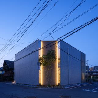 夜になると、隅切り部分に仕込まれた縦の間接照明が壁面を照らし出す。看板もなく閉ざされた佇まいは、通りかかった人に「何の建物だろう」という印象を残す。