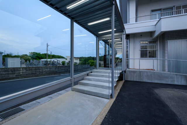 緩やかなスロープや増築部の緩やかな段差とあわせ、入り口の階段部もかなり緩やかなものとした。外と中の連続性を持たせた意匠だ。歩行する際の安定性や安心感、緩やかな表情を入り口に持たせる意図もある