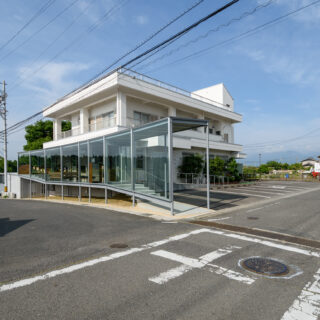外観。敷地の角まで増築部があるため、受け壁もガラスとした。写真左の道から来た車が写真右側へ左折する際、人や車の交通状況がわかるようにと配慮した結果だ。全面ガラスの側面との連続性をあわせ持つ、違和感のないデザインとなっている