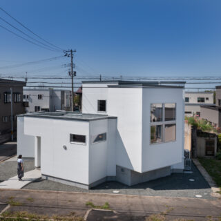 隣家に日差しが入り、近隣へ圧迫感を与えないように屋根の高さを低くした。周囲への配慮だ。リビングが飛び出して宙に浮いているように見えるのは、箱が集まっている印象を強く出すため。玄関の左にはお客様用の駐車スペースが用意されている