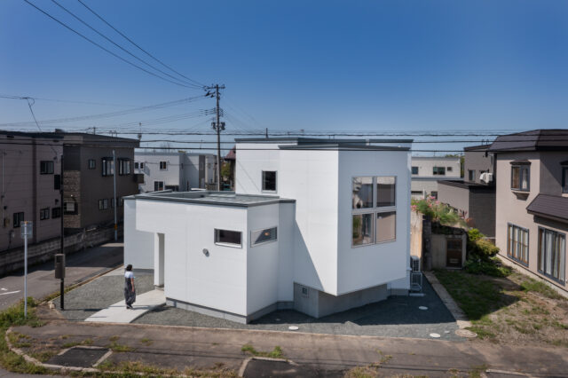 隣家に日差しが入り、近隣へ圧迫感を与えないように屋根の高さを低くした。周囲への配慮だ。リビングが飛び出して宙に浮いているように見えるのは、箱が集まっている印象を強く出すため。玄関の左にはお客様用の駐車スペースが用意されている