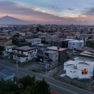 上空から。津軽富士と呼ばれる岩木山を遠方に望む住宅地。独創的な外観が目を引く。外壁が白い影響で建物が大きく見えるため、屋根を低く抑えていることがわかる
