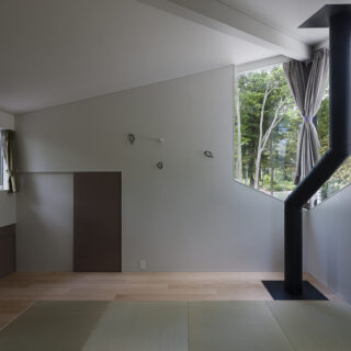 2階、お子さまたち家族のための寝室。正面の扉は小屋裏収納だが、現在はそこも畳敷きとし寝室として使用している。窓からは北方向の眺めが楽しめる。季節によって浅間山も見えるという。窓の前、室内を薪ストーブの煙突が通る。煙突表面は触れてもやけどをしない仕様となっている