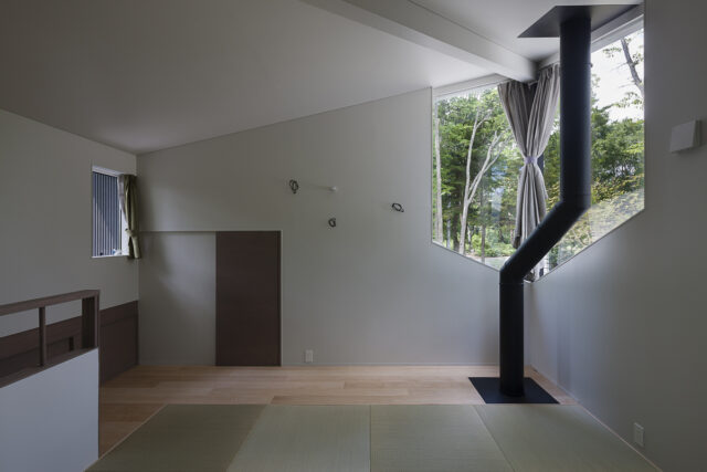 2階、お子さまたち家族のための寝室。正面の扉は小屋裏収納だが、現在はそこも畳敷きとし寝室として使用している。窓からは北方向の眺めが楽しめる。季節によって浅間山も見えるという。窓の前、室内を薪ストーブの煙突が通る。煙突表面は触れてもやけどをしない仕様となっている