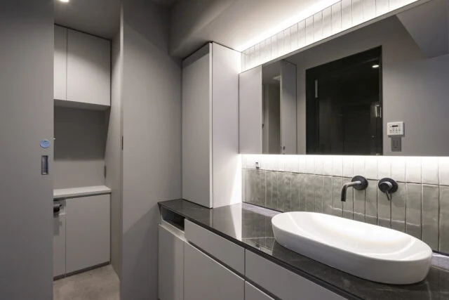 手洗い・浴室・トイレが集まり、動線に配慮された水回り。このエリアもすべて造作家具だ。手洗いの天板は対面カウンターの天板を作った時の端材。同じ素材なので統一感も感じられる。配色は汚れが目立たず、落ち着いた空間とするためにグレーで統一した